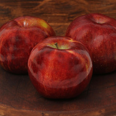 Three red apples on wooden table, selective focus