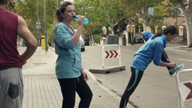Young people stretching, drinking and jogging in city