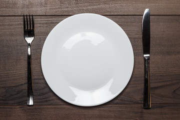 white plate with knife and fork on wooden table