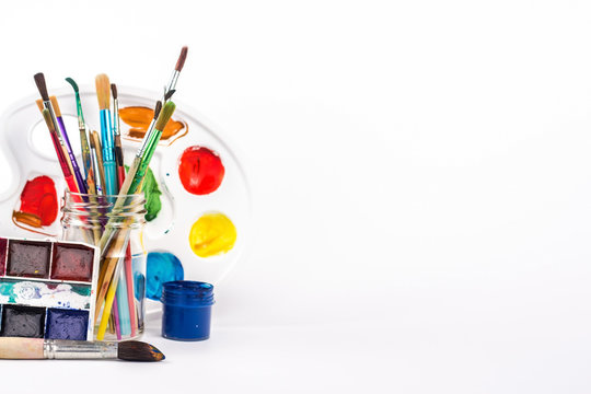 isolated paint palette and paints brushes in glass