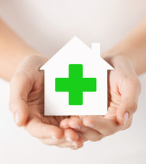 hands holding paper house with green cross