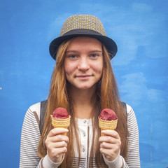 Funny hipster girl with ice cream in hand on the blue wall.