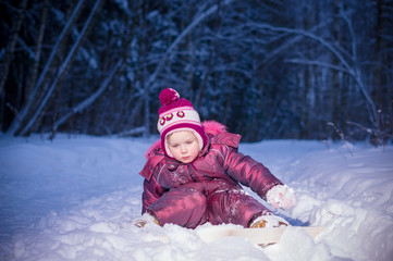 Fototapeta na wymiar Adorable girl ride on ski in evening park. Sit on snow