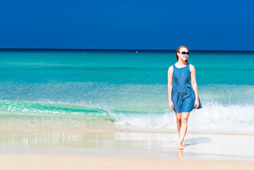 Fototapeta na wymiar Young woman wearing a blue dress walking on a beach