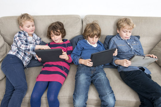 Brothers And Sister Using Digital Tablets On Sofa