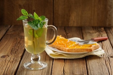 Mint tea and toasts with orange marmalade on wooden background