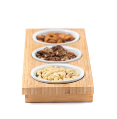 Set of assorted nuts in white bowls on wooden stand. Isolated