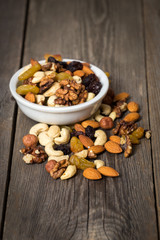 Assorted nuts in white bowl on wooden background.
