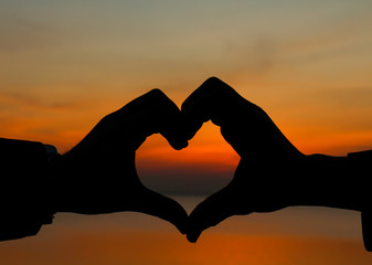 Hands making heart shape with sun in center and cloudy blue sky