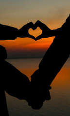 Hands making heart shape with sun in center and cloudy blue sky