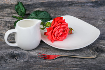 dishes, milk jug and rose on the wooden background
