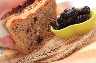 Slicing fresh bread, dried plums and ears of wheat