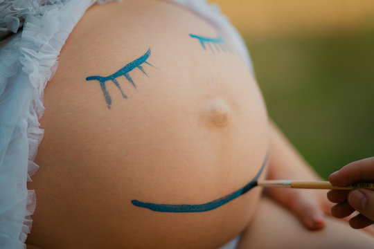 Pregnant woman belly closeup with smiling funny face drawing