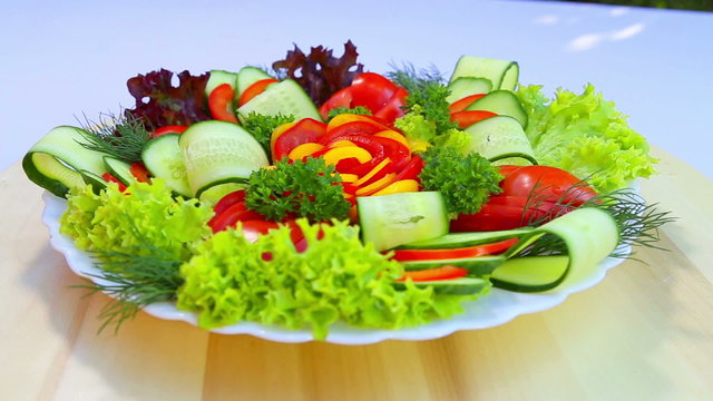 Cutting a variety of fresh, juicy vegetables on a white plate.