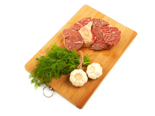 A large piece of red meat, dill and garlic on a wooden board on