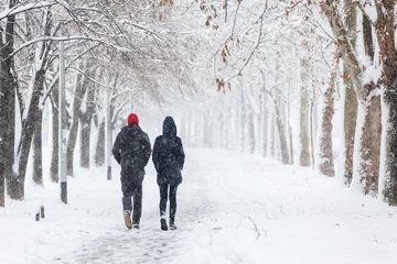 Fotobehang Winter Paar wandelen tijdens zware sneeuwstorm op het steegje onder boom