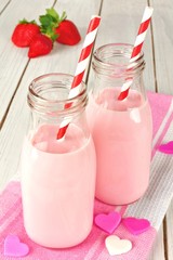 Strawberry milk in bottles with hearts on wood table