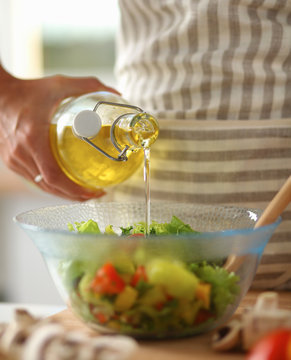 Smiling young woman  mixing fresh salad, holding bottle of oil