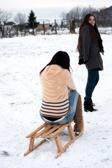 Two girlfriends sledge downhill in winter