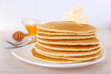 Stack of delicious pancakes with butter and honey in saucer