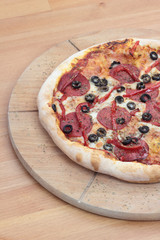 Closeup of pizza with salami, peperoni, black olives and pepper.