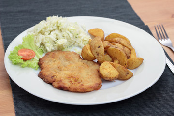 Wiener schnitzel with fried potato wedges and cabbage salad.