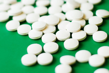 Fototapeta na wymiar White pills on green background, differential focus