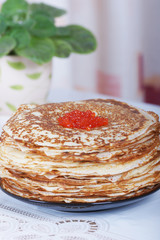 Банка красной икры на фоне большой стопки блинов на столе