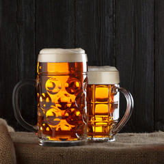 Beer glasses on table with burlap cloth, dark wooden background