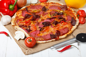 Pizza with ham, salami and chili pepper, on wooden table