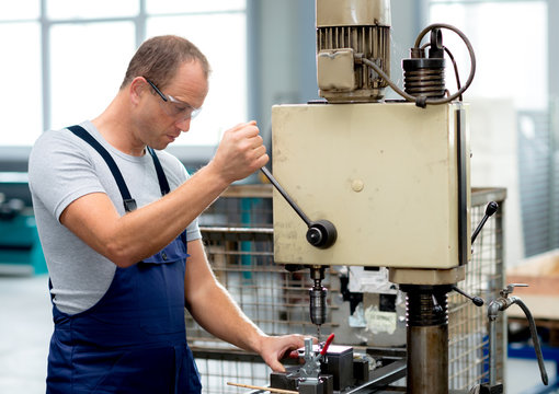 young worker in factory using drill machine