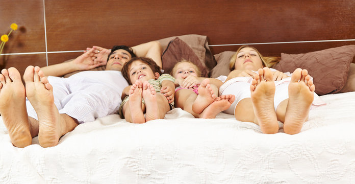 Familie liegt im Bett mit F&uuml;&szlig;en nach vorne