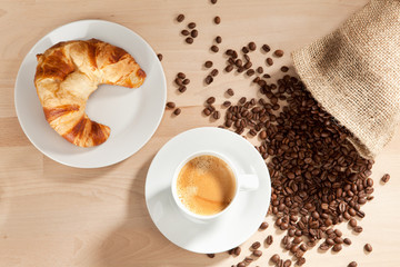 Kaffee und Croissant mit Kaffeebohnen aus dem Jutesack