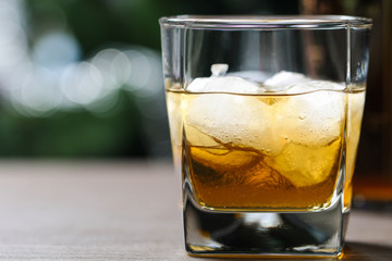 glass with whiskey and ice on wooden table