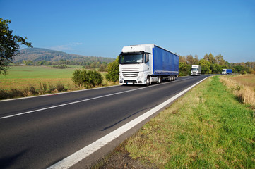 Obraz na płótnie Canvas Three white trucks on the road in the countryside