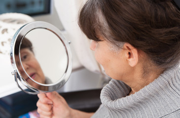 Obraz premium Pension age good looking woman looking in mirror 