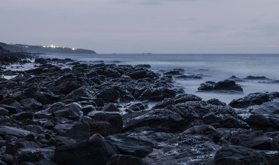 Twilight rocky seascape with lights in background