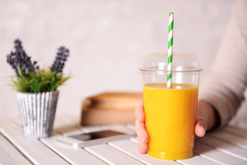Female hand at wooden table with fast food closed cup of orange