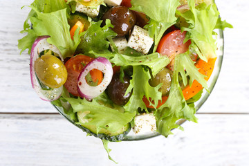 Greek salad in glass dish on color wooden table background