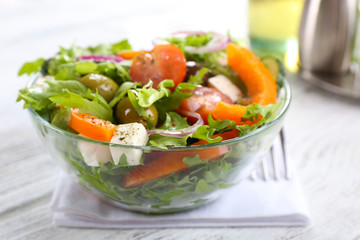Greek salad in glass dish on napkin and color wooden background