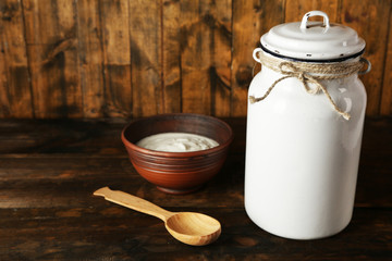 Milk can with cream on rustic wooden background