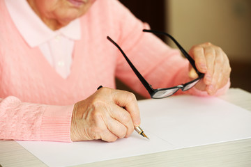 Hands of adult woman writing with pen and glasses,