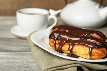 Tasty eclairs and cup of tea on wooden table