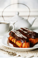 Tasty eclairs and cup of tea on wooden table