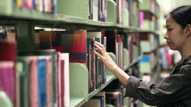 Female, girl student walking between shelves, searching for book