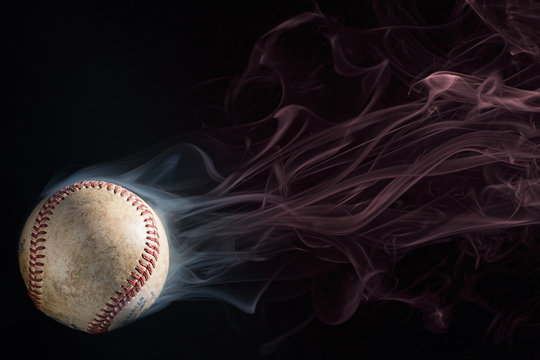 Baseball on black ground with white smoke coming off of it, which then turns to red smoke. Copy Space above the ball.