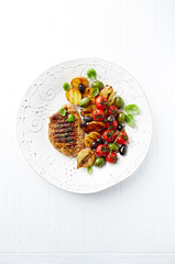 Grilled pork steak with vegetables and fresh basil leaves on a p