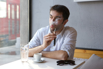 Young man sitting indoors smoking electric cigarette