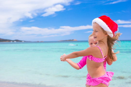 Little adorable girls in Santa hats during beach vacation