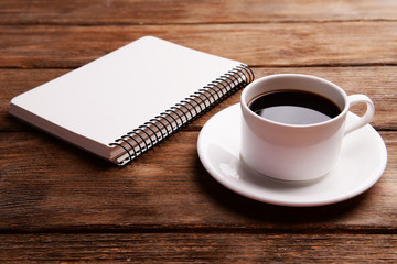 Cup of coffee on saucer with notebook on wooden table